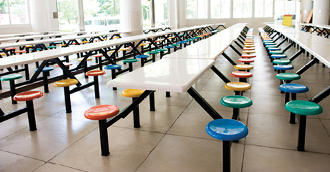 Empty school cafeteria featuring six rows of white tables with seats