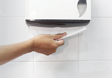 Hand pulling folded paper towels from a restroom towel dispenser