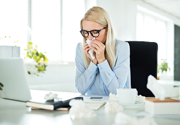 Woman in an office environment wiping her nose with facial tissue